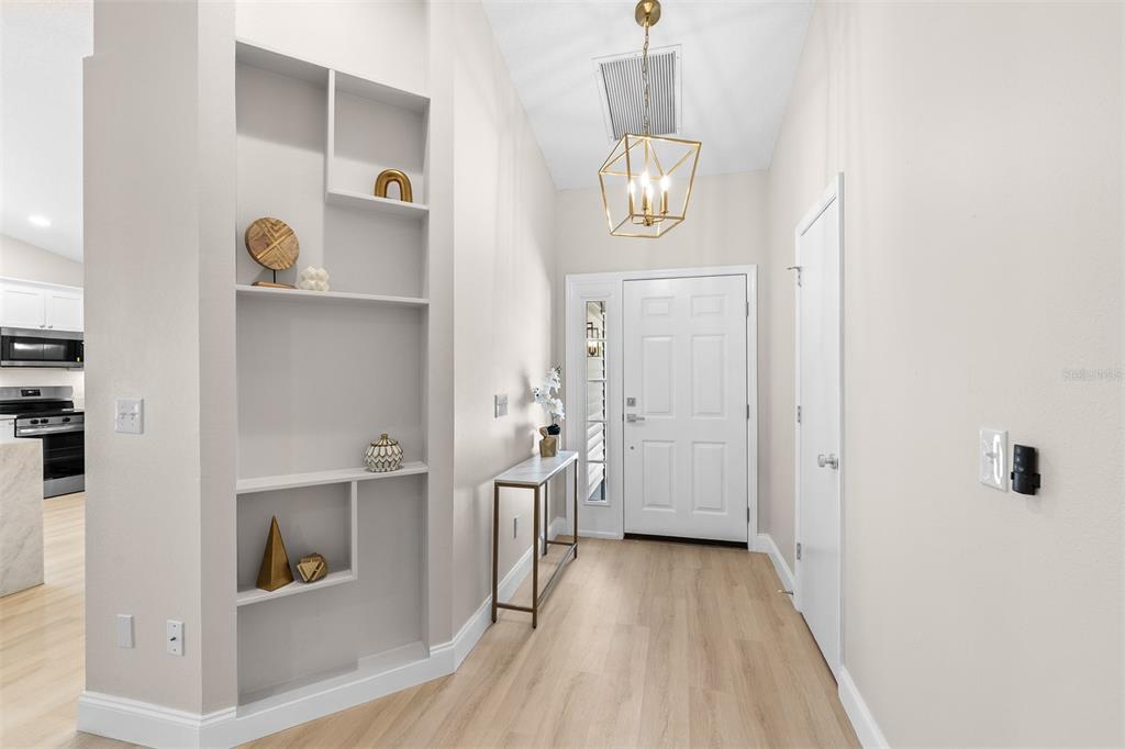 An entryway features light wood flooring, a built-in shelving unit, and a modern geometric chandelier — 6572 ABERCROMBIE COURT, ORLANDO, FL