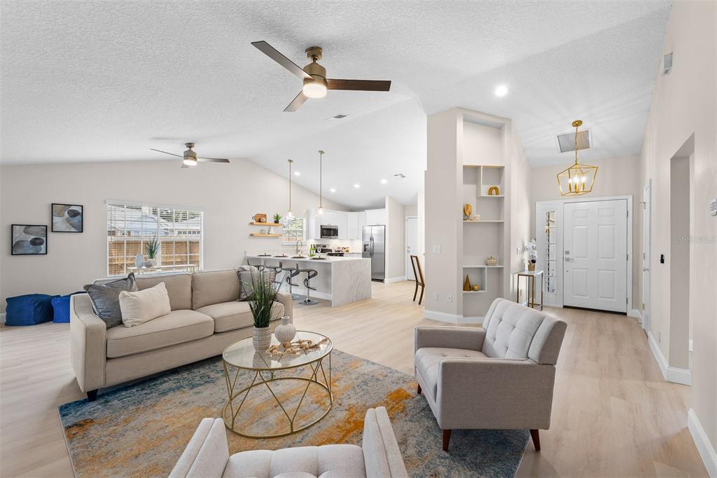 An open-concept living room and kitchen featuring light wood floors, neutral walls, and modern furniture — 6572 ABERCROMBIE COURT, ORLANDO, FL