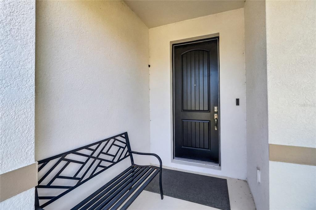 A black metal bench sits on a covered porch next to a black front door — 13520 PALMERA VISTA DRIVE, RIVERVIEW, FL