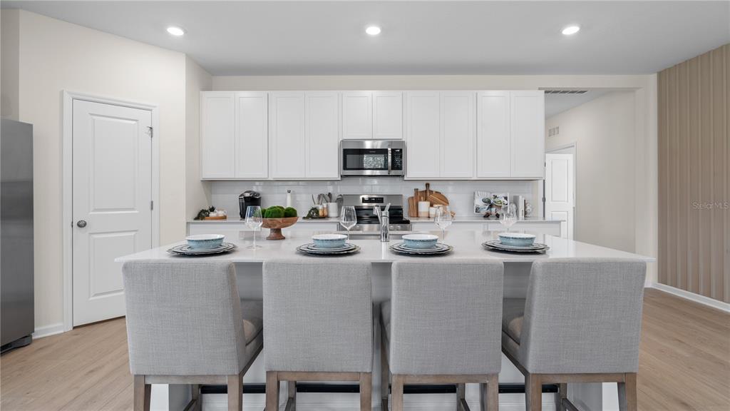 A modern kitchen features white cabinets, a large island with four chairs, and stainless appliances — 3146 MINDFULLNESS DRIVE, CLERMONT, FL