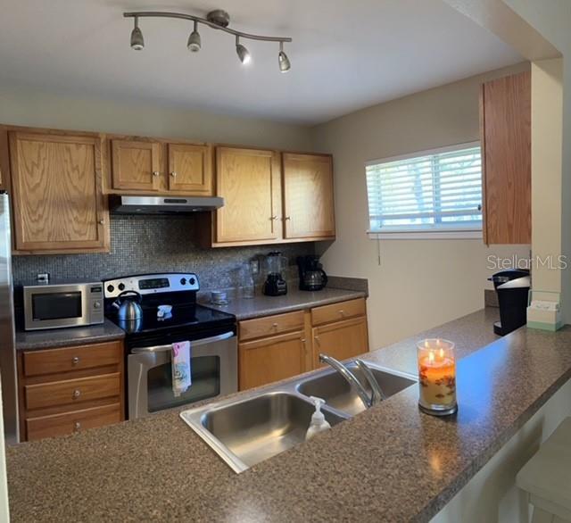 A kitchen features wood cabinets, stainless steel appliances, a double sink, and a breakfast bar — 1818 PARAKEET WAY UNIT 1001, SARASOTA, FL
