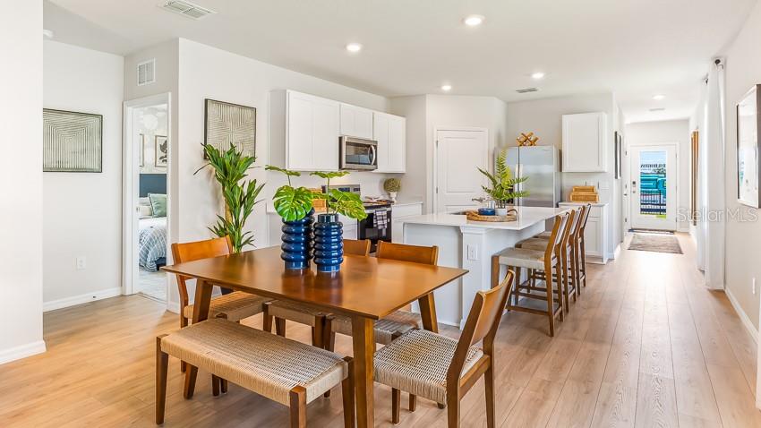 An open-concept kitchen and dining area features light wood flooring, white cabinetry, and a kitchen island — 11857 TEXOMA COURT, PARRISH, FL
