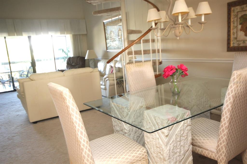 A dining area with a glass table and chairs sits before a spiral staircase — 1255 DOCKSIDE PLACE UNIT 211, SARASOTA, FL