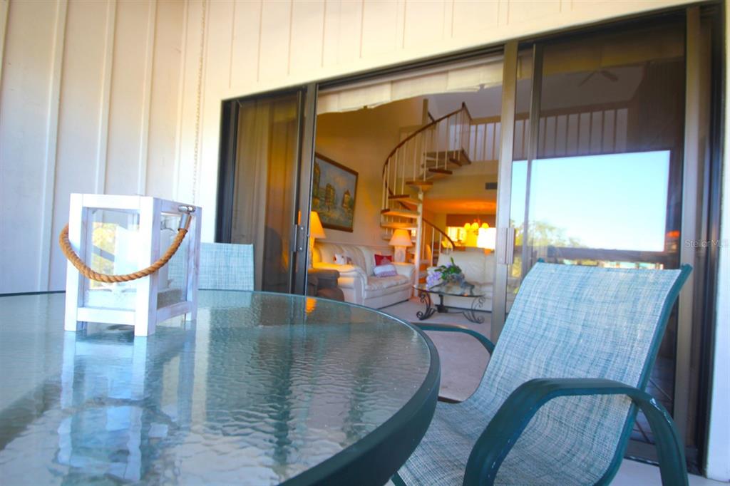A glass-topped patio table and chairs sit outside a sliding door leading to a living room — 1255 DOCKSIDE PLACE UNIT 211, SARASOTA, FL