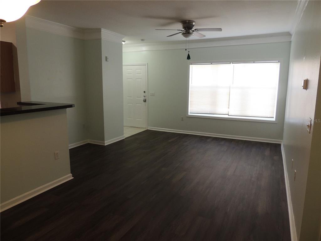 An empty living room features dark wood-look flooring, light-colored walls, a ceiling fan, and a window — 4802 51ST STREET W UNIT 1109, BRADENTON, FL