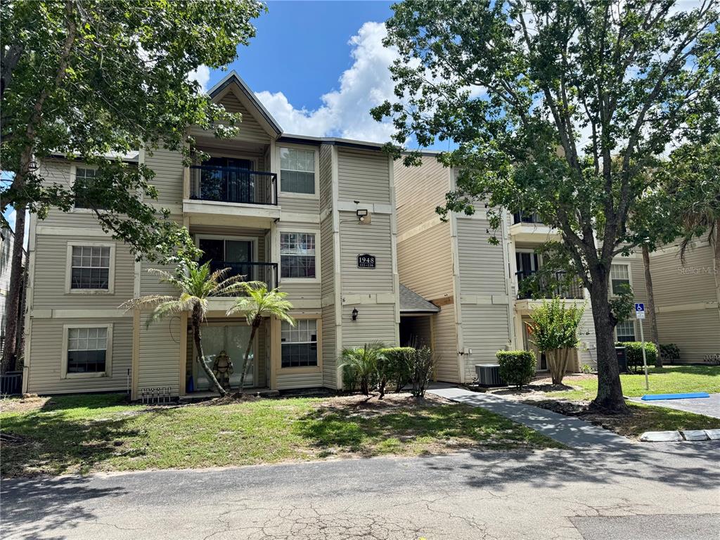 A three-story apartment building with beige siding and balconies surrounded by trees and grass — 1948 LAKE ATRIUMS CIRCLE UNIT 119, ORLANDO, FL
