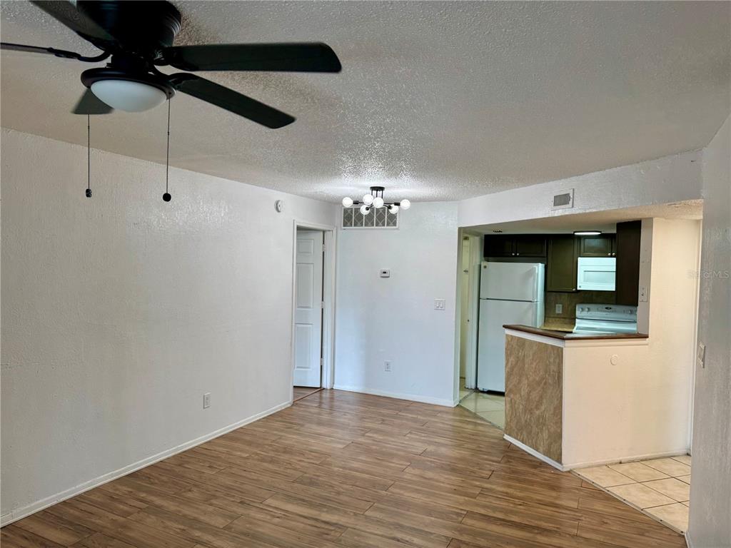 A living room with wood-look flooring, a ceiling fan, and an adjacent kitchen with cabinets — 1948 LAKE ATRIUMS CIRCLE UNIT 119, ORLANDO, FL