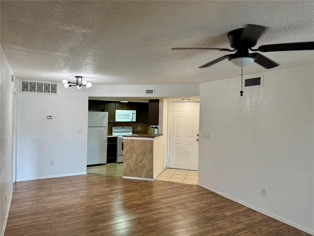 An open-concept living area features wood-look flooring, a ceiling fan, and an adjacent kitchen — 1948 LAKE ATRIUMS CIRCLE UNIT 119, ORLANDO, FL