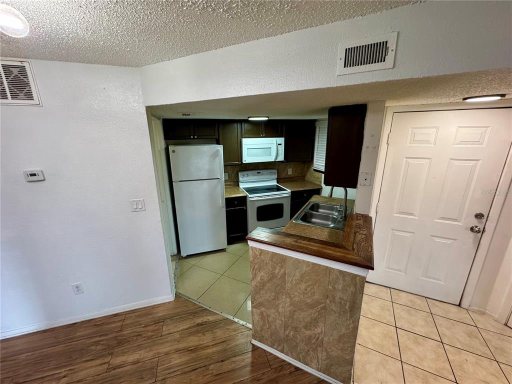A kitchen with white appliances, dark cabinets, and a tiled breakfast bar area — 1948 LAKE ATRIUMS CIRCLE UNIT 119, ORLANDO, FL
