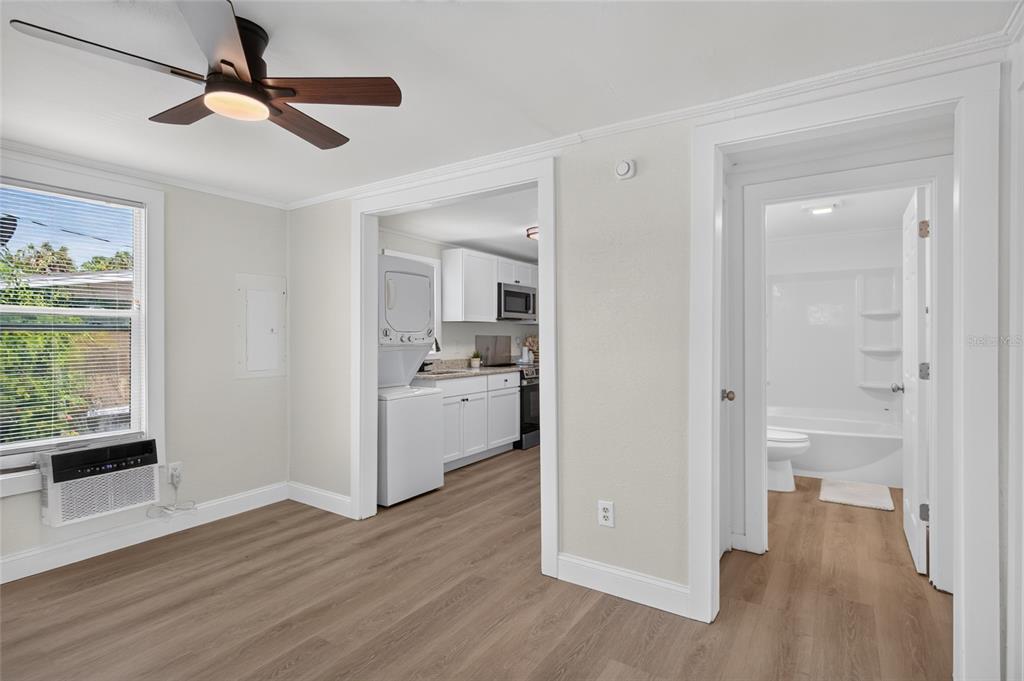 A room with wood-look flooring, a ceiling fan, a window unit, and doorways to a kitchen — 1545 29TH STREET, SARASOTA, FL