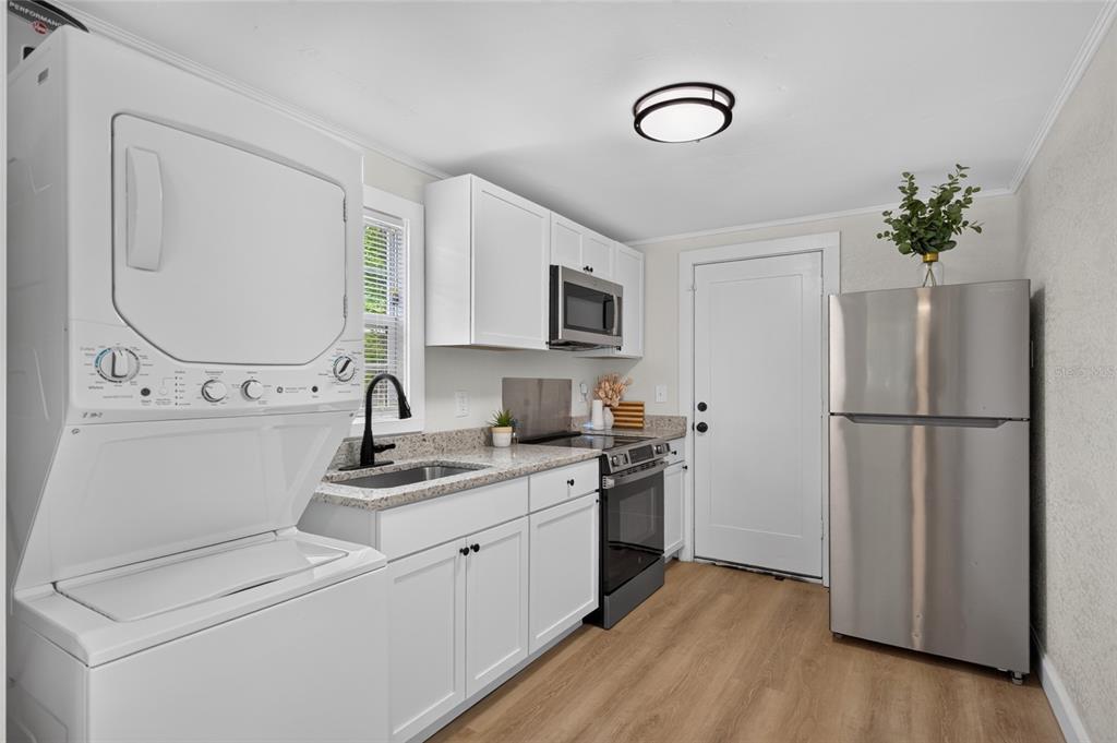 A kitchen features white cabinets, stainless steel appliances, a stacked washer-dryer, and light wood flooring — 1545 29TH STREET, SARASOTA, FL