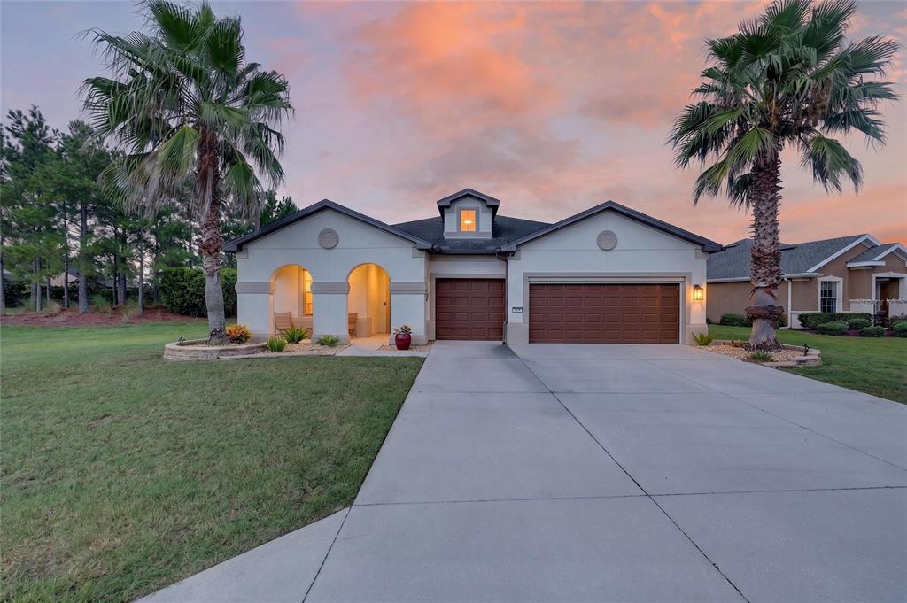 A single-story house with a two-car garage, arched entryway, and two palm trees at sunset — 9712 SW 75TH STREET RD, OCALA, FL