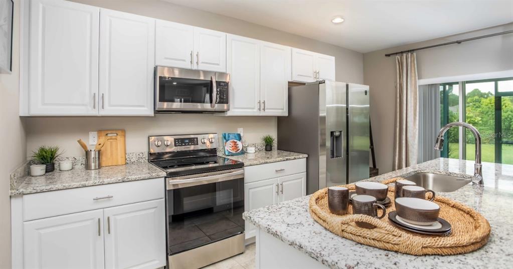 A kitchen features white cabinets, granite countertops, stainless steel appliances, and a central island — 11007 BAYLOR DRIVE, SPRING HILL, FL