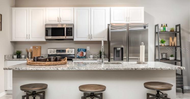 A kitchen features white cabinets, stainless steel appliances, a granite island, and three wooden stools — 11007 BAYLOR DRIVE, SPRING HILL, FL