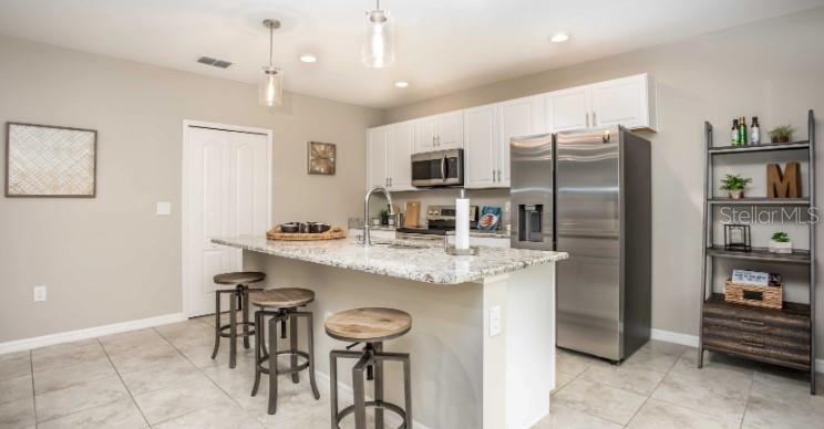 A kitchen features a granite-topped island with three stools, white cabinetry, and stainless steel appliances — 11007 BAYLOR DRIVE, SPRING HILL, FL