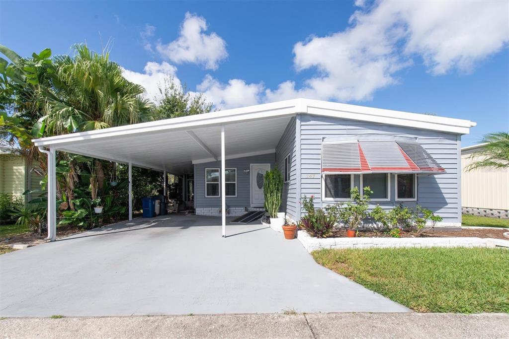 A light blue mobile home features a large carport, a front lawn, and metal awnings — 347 CANAL WAY, OLDSMAR, FL