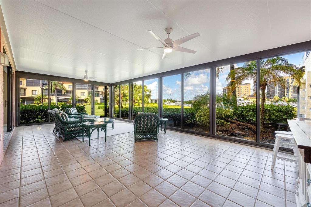 A tiled sunroom features a ceiling fan, wicker furniture, and large windows overlooking a marina — 3250 SOUTHSHORE DRIVE UNIT 55A, PUNTA GORDA, FL