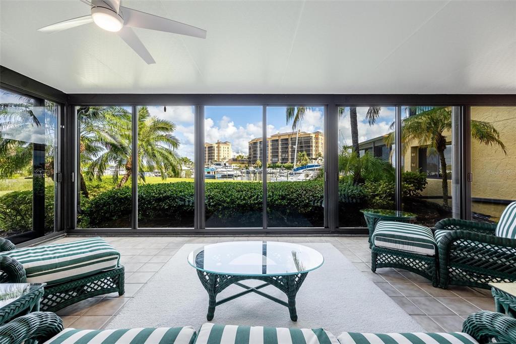 A sunroom with wicker furniture, tile floors, and large windows overlooking a marina and buildings — 3250 SOUTHSHORE DRIVE UNIT 55A, PUNTA GORDA, FL