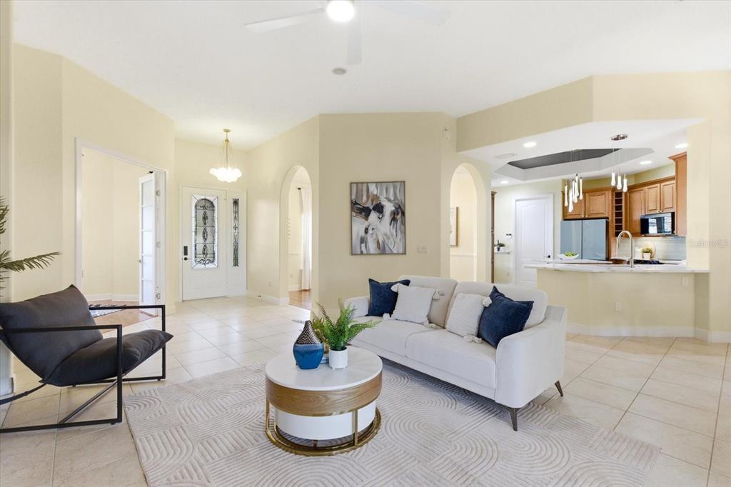 An open-concept living room features tile flooring, a white sofa, and an adjacent kitchen area — 1064 CEASARS COURT, MOUNT DORA, FL
