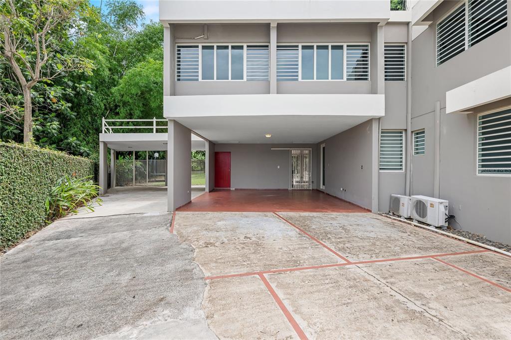 A concrete driveway leads to a covered parking area under a two-story gray building — 2 CALLE 2 TINTILLO HILLS UNIT 606, GUAYNABO, PR