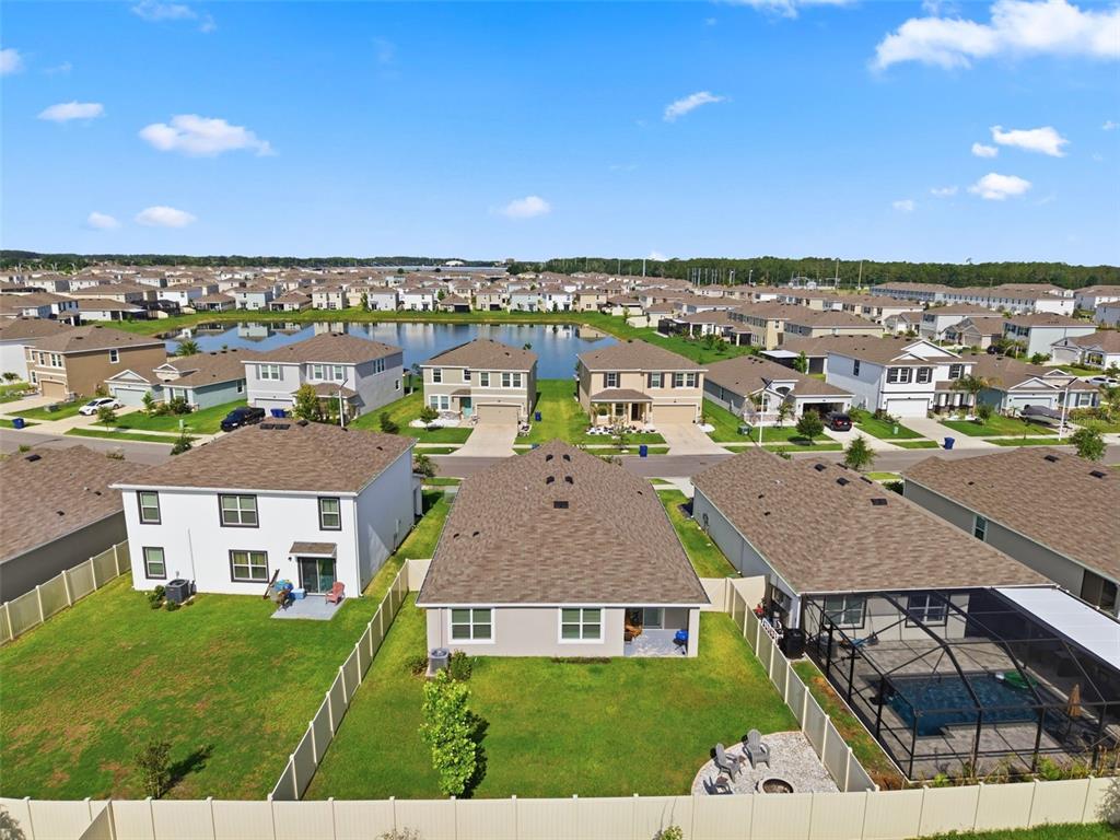 An aerial view shows suburban houses with backyards, a central pond, and clear blue skies — 9014 FORGE BREEZE LOOP, WESLEY CHAPEL, FL