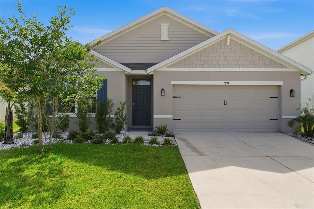 A single-story suburban house with a beige exterior, a two-car garage, and a front lawn — 9014 FORGE BREEZE LOOP, WESLEY CHAPEL, FL