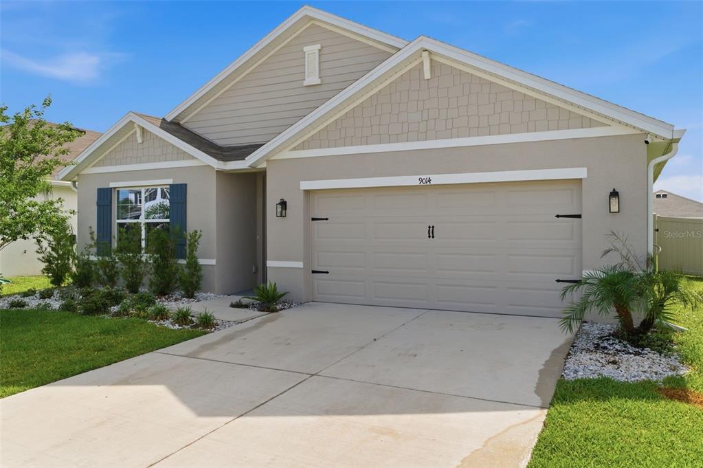 A single-story suburban house with a beige stucco exterior, a two-car garage, and blue shutters — 9014 FORGE BREEZE LOOP, WESLEY CHAPEL, FL