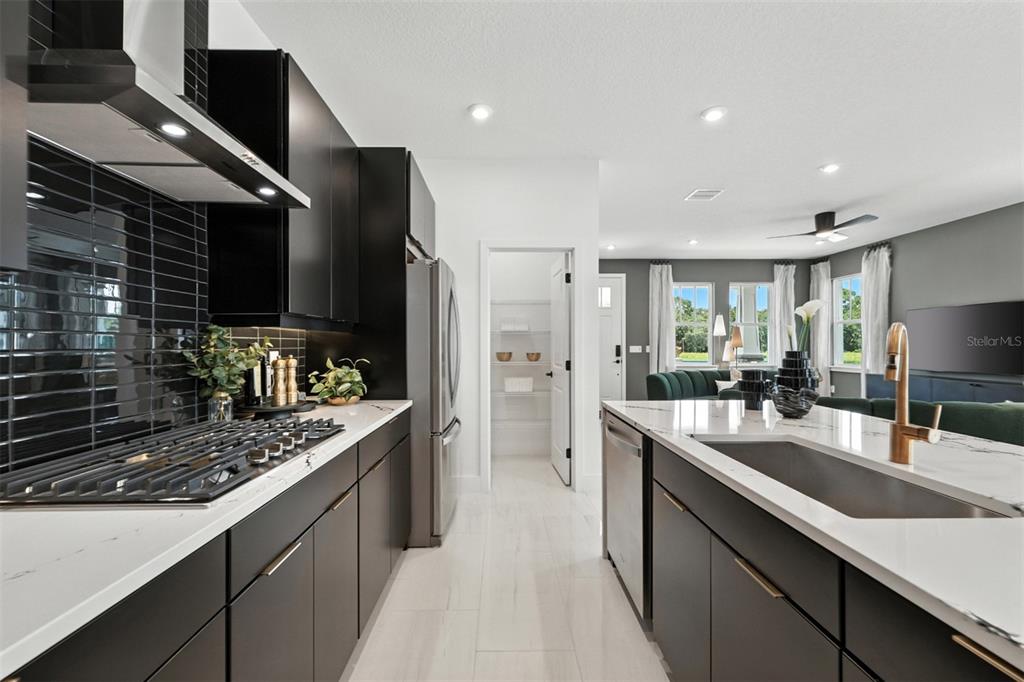 A modern kitchen features black cabinetry, white countertops, a gas range, and a walk-in pantry — 1796 HEADLAND LOOP, CELEBRATION, FL