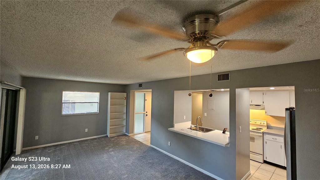 A living room with gray carpet, a ceiling fan, and an open pass-through to the kitchen — 7 CASTANIA COURT, ST AUGUSTINE, FL