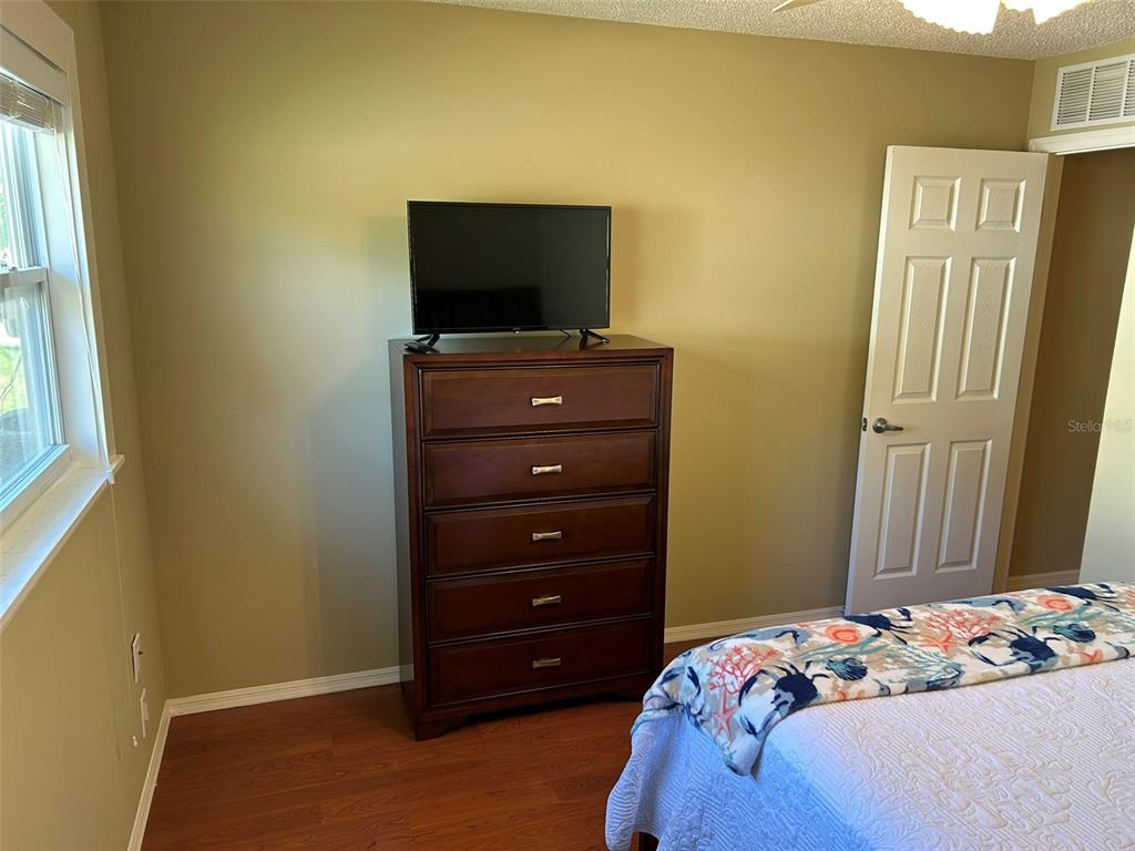A bedroom features a wooden dresser with a television, a white door, and wood flooring — 3424 UNITY TREE DRIVE, EDGEWATER, FL