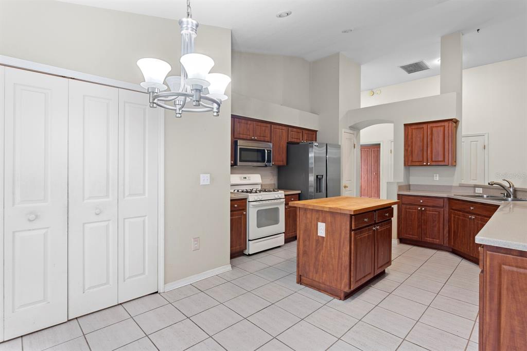 A kitchen with wood cabinets, a wooden island, stainless steel appliances, and light tile flooring — 10420 SPRINGROSE DRIVE, TAMPA, FL