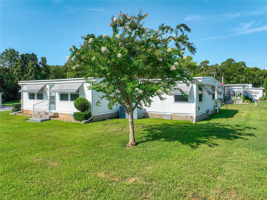 A white mobile home with a metal roof sits on a grassy lawn with trees — 1925 BROOKSIDE DRIVE, MOUNT DORA, FL