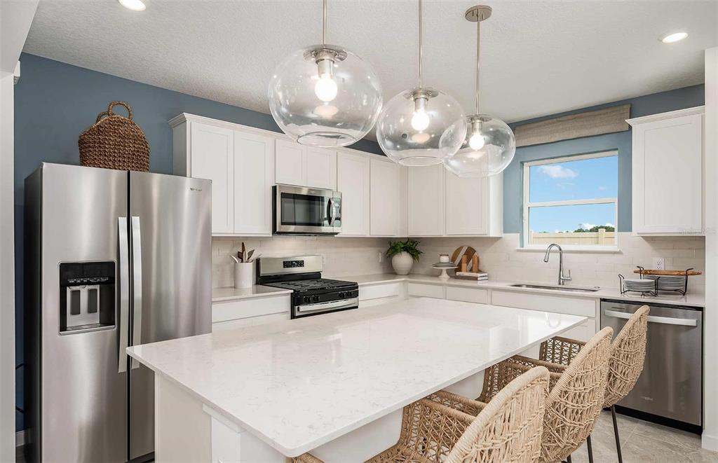 A modern kitchen features white cabinets, a large quartz island, and three glass pendant lights — 9181 NEWMONS PLACE, WILDWOOD, FL