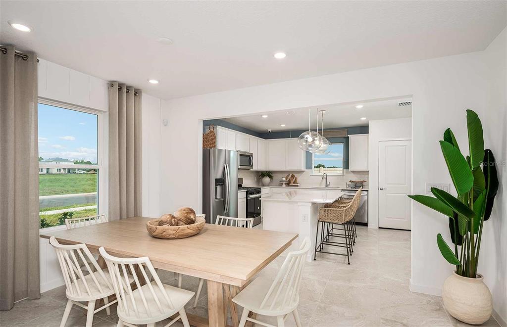 A dining area with a wooden table and white chairs opens into a modern kitchen — 9181 NEWMONS PLACE, WILDWOOD, FL