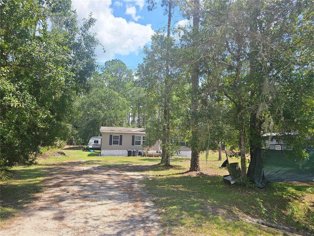 A tan mobile home sits on a grassy lot surrounded by trees under a blue sky — 1387 WATER OAK ROAD, BUNNELL, FL