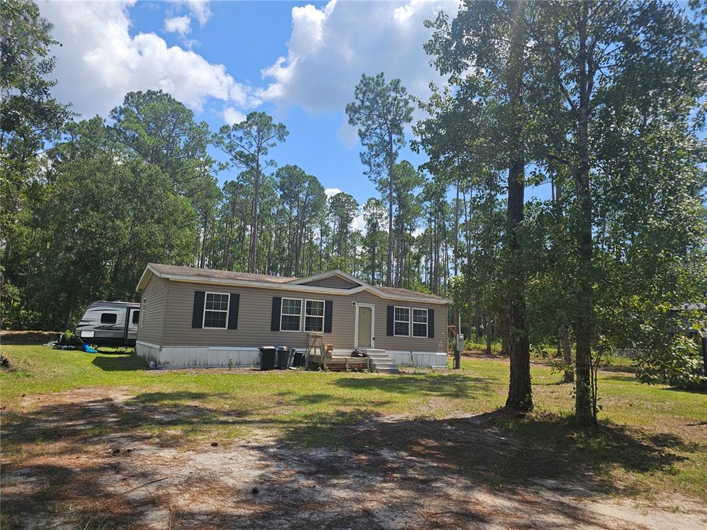 A single-story manufactured home with tan siding sits on a wooded lot — 1387 WATER OAK ROAD, BUNNELL, FL