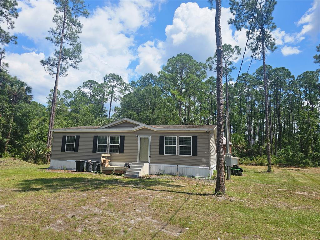 A single-story manufactured home with tan siding sits on a grassy lot surrounded by trees — 1387 WATER OAK ROAD, BUNNELL, FL