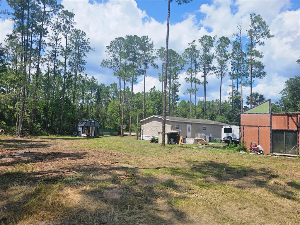 A grassy yard features a mobile home, a small shed, and an unfinished wooden structure — 1387 WATER OAK ROAD, BUNNELL, FL