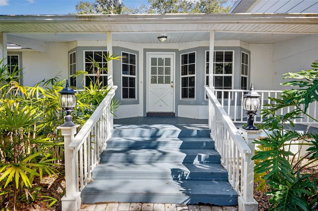A white house entrance features a blue wooden staircase leading to a glass-paneled front door — 4875 SAILFISH DRIVE, PONCE INLET, FL