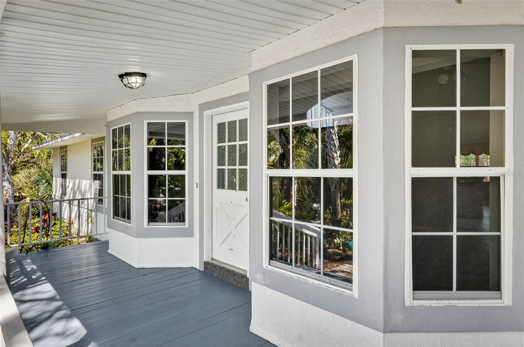 A covered porch with gray decking features a white door and several multi-pane windows — 4875 SAILFISH DRIVE, PONCE INLET, FL