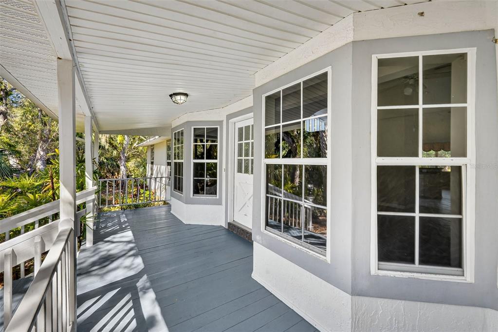 A covered wooden porch with white railings leads to a white door and bay windows — 4875 SAILFISH DRIVE, PONCE INLET, FL