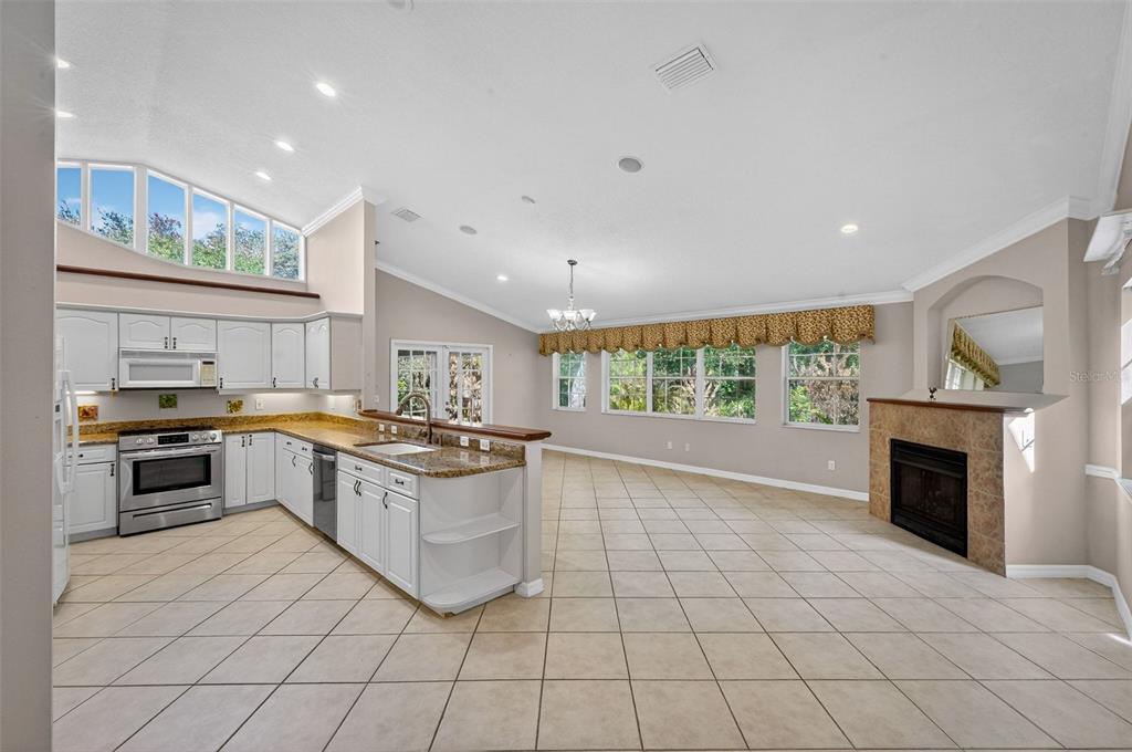 An open-concept kitchen and living area with white cabinets, tile floors, and a stone fireplace — 4875 SAILFISH DRIVE, PONCE INLET, FL