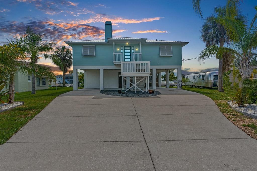 A light blue elevated house with a concrete driveway and a metal roof at sunset — 4464 JACONA DRIVE, HERNANDO BEACH, FL