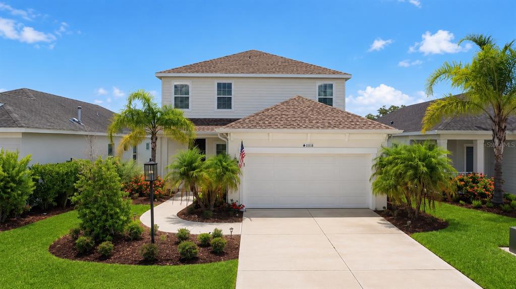 A two-story suburban house features a white garage, a concrete driveway, and palm trees — 11118 SAND PINE LANE, PARRISH, FL