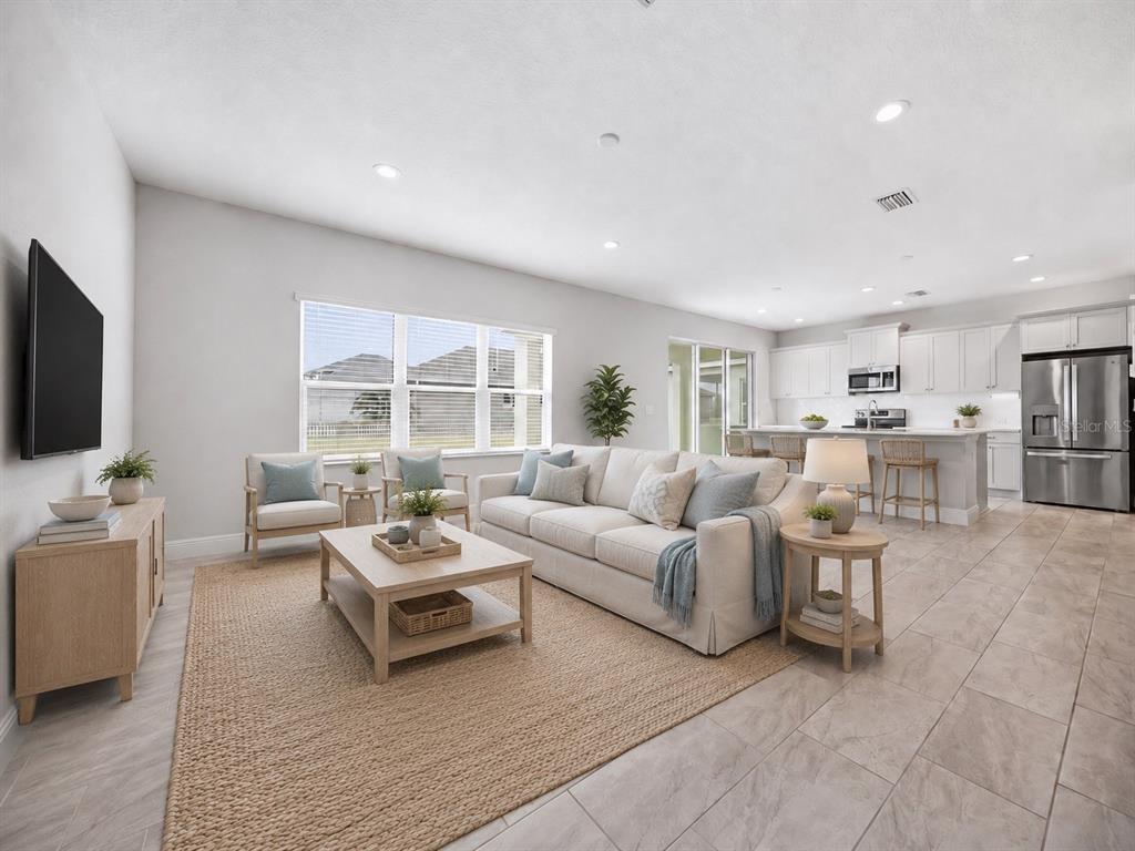 A bright, open-concept living room with a neutral sofa, coffee table, and adjacent kitchen area — 11118 SAND PINE LANE, PARRISH, FL