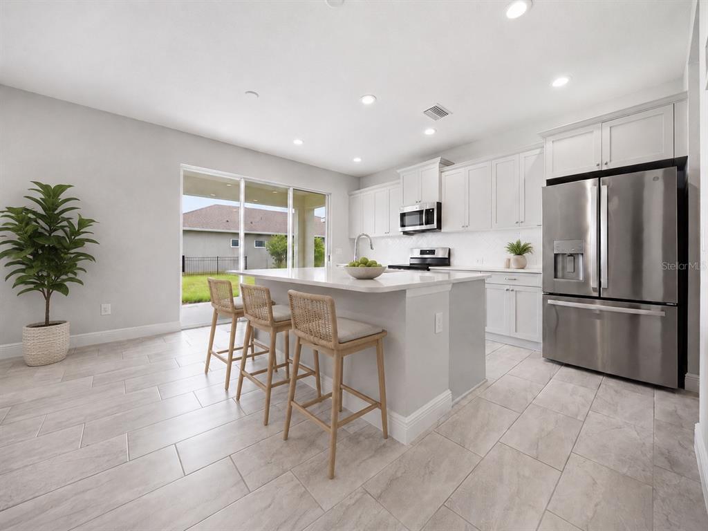 A modern kitchen features white cabinetry, a central island with bar stools, and tile flooring — 11118 SAND PINE LANE, PARRISH, FL
