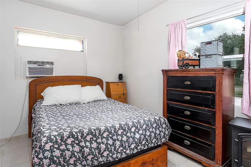 A bedroom features a bed with a floral comforter, a wooden dresser, and a window unit — 7008 TRIPOLI WAY, ORLANDO, FL