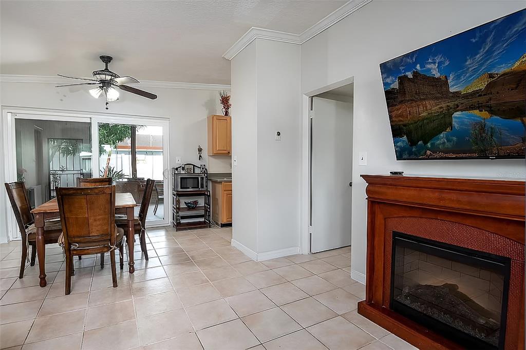 A dining area with tile floors, a ceiling fan, and a fireplace with a mounted television — 7008 TRIPOLI WAY, ORLANDO, FL