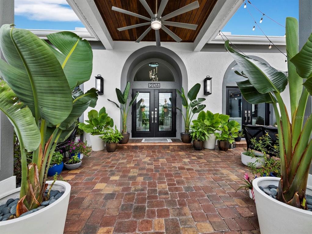A covered brick patio features large potted plants, double glass doors, and a ceiling fan — 206 FOUR KNOT LANE, OSPREY, FL