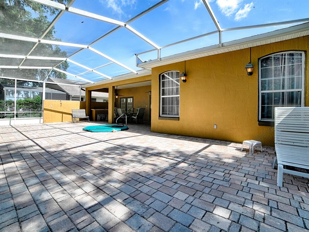 A paved patio enclosed by a screen cage features a yellow wall and outdoor furniture — 830 OLD OAKS LANE, LEESBURG, FL